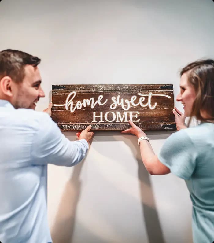 A smiling couple placing a wooden "home swwt home" plate at their new home