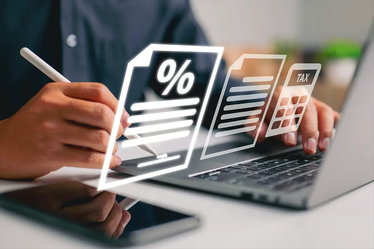 An accountant working with a laptop and pencil on taxes with icons coming out of the screen